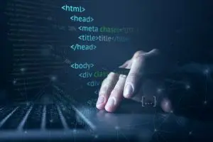 Mano sobre teclado portátil con líneas de código HTML en pantalla, simbolizando desarrollo web y programación